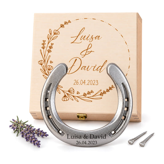 Glückshufeisen aus Stahl mit Gravur „Luisa & David 26.04.2023“ vor gravierter Holz-Geschenkbox mit Blumenkranz, Lavendel und zwei Hufnägeln