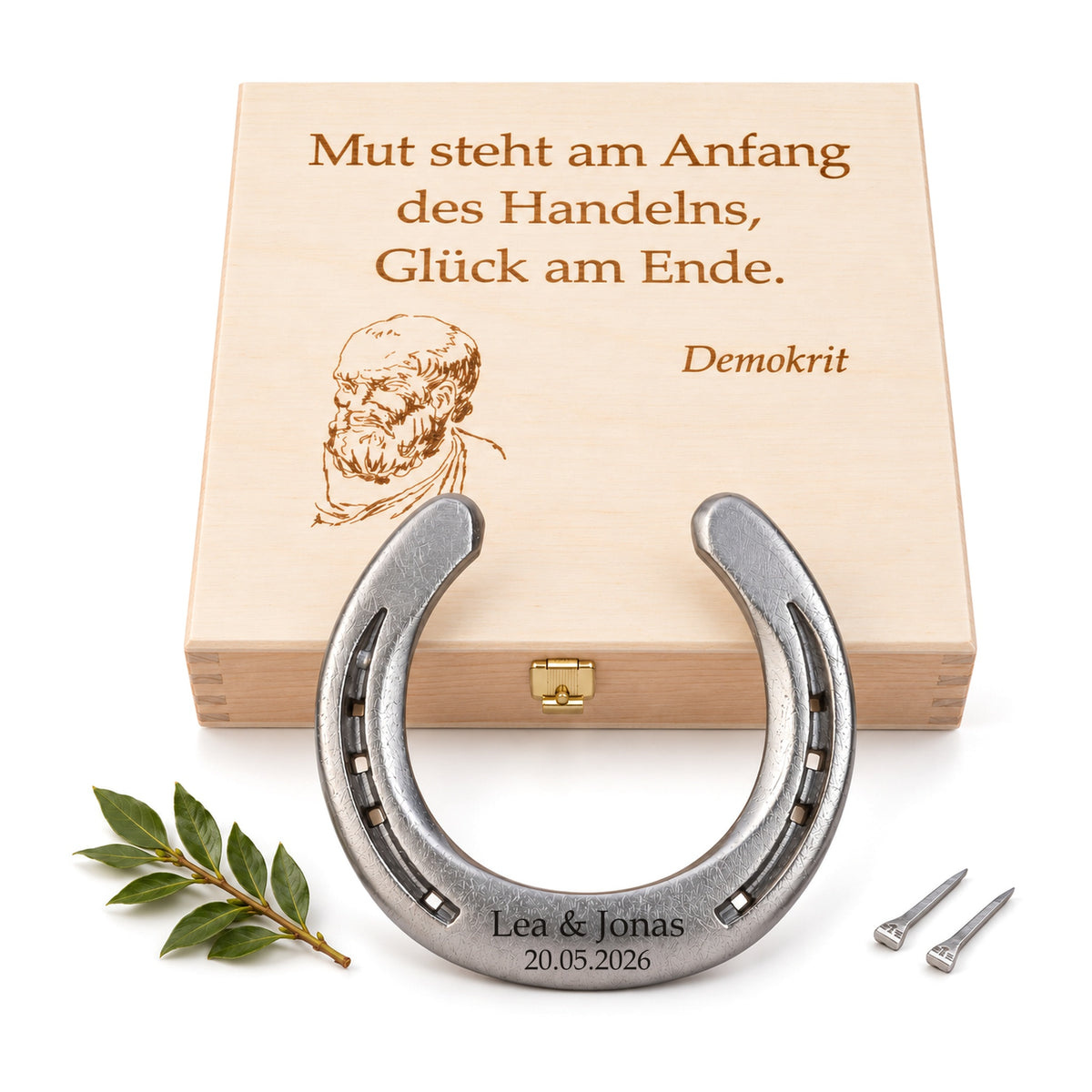 Glückshufeisen aus Stahl mit Gravur „Lea & Jonas 20.05.2026“ vor Holz-Geschenkbox mit Demokrit-Zitat und Porträt, Lorbeerzweig und zwei Hufnägeln