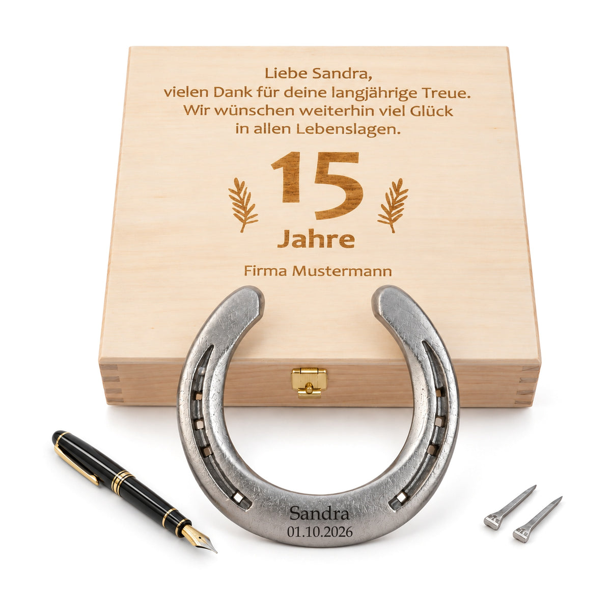 Glückshufeisen aus Stahl mit Gravur „Sandra 01.10.2026“ vor Holz-Geschenkbox mit graviertem Wunschtext zum 15-jährigen Firmenjubiläum, Füllfederhalter und zwei Hufnägeln