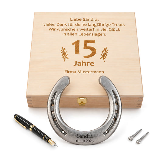 Glückshufeisen aus Stahl mit Gravur „Sandra 01.10.2026“ vor Holz-Geschenkbox mit graviertem Wunschtext zum 15-jährigen Firmenjubiläum, Füllfederhalter und zwei Hufnägeln