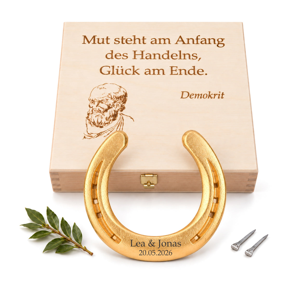 Vergoldetes Glückshufeisen (24 Karat) mit Gravur „Lea & Jonas 20.05.2026“ vor Holz-Geschenkbox mit Demokrit-Zitat und Porträt, Lorbeerzweig und zwei Hufnägeln