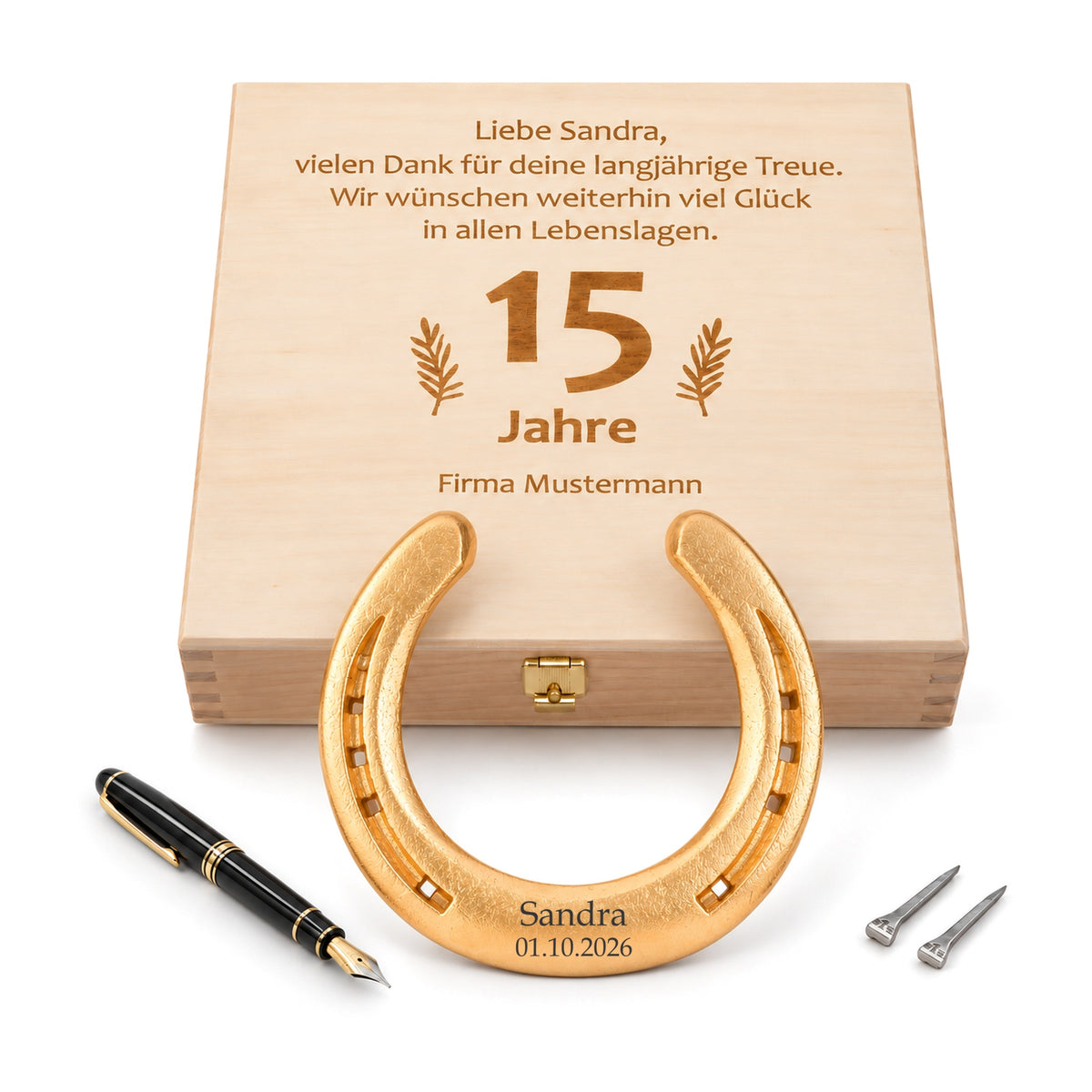 Vergoldetes Glückshufeisen (24 Karat) mit Gravur „Sandra 01.10.2026“ vor Holz-Geschenkbox mit graviertem Wunschtext zum 15-jährigen Firmenjubiläum, Füllfederhalter und zwei Hufnägeln
